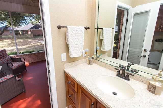 bathroom with a textured wall, vanity, and toilet