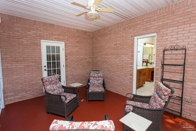 living area with ceiling fan and brick wall