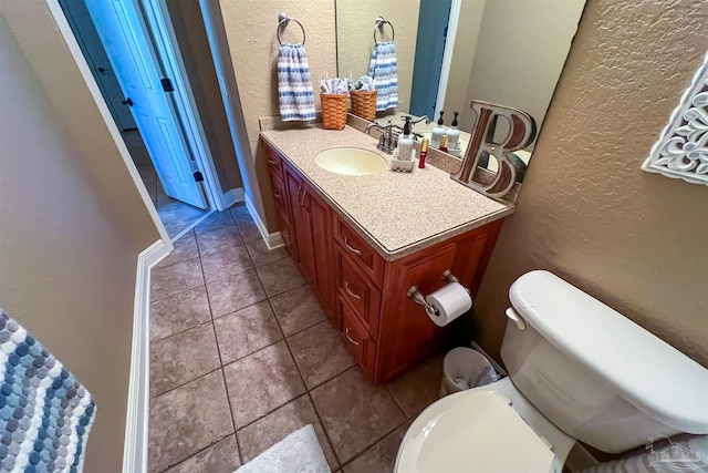 bathroom featuring a textured wall, toilet, vanity, baseboards, and tile patterned floors