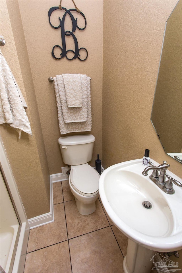 bathroom with toilet, a textured wall, a sink, and tile patterned floors