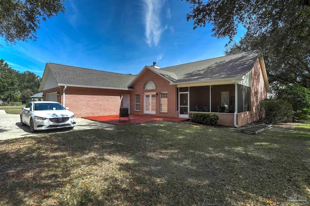 back of house with an attached garage, brick siding, a sunroom, a yard, and a chimney