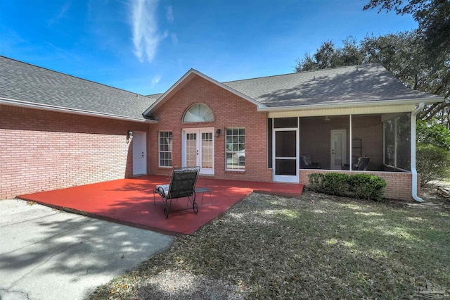 rear view of house featuring a shingled roof, a sunroom, brick siding, and a patio