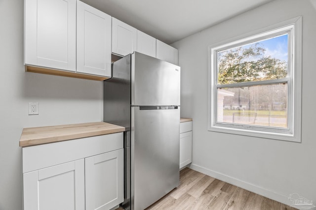 kitchen featuring white cabinetry, plenty of natural light, wooden counters, and stainless steel refrigerator