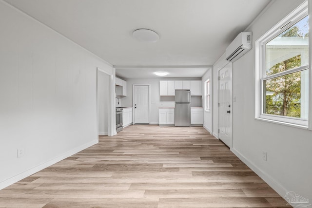 kitchen with stainless steel refrigerator, range, white cabinetry, a wall mounted air conditioner, and light hardwood / wood-style floors