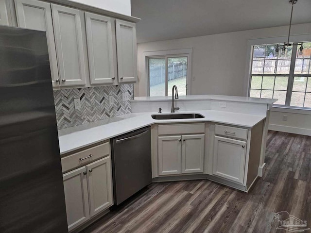 kitchen with pendant lighting, appliances with stainless steel finishes, sink, backsplash, and kitchen peninsula