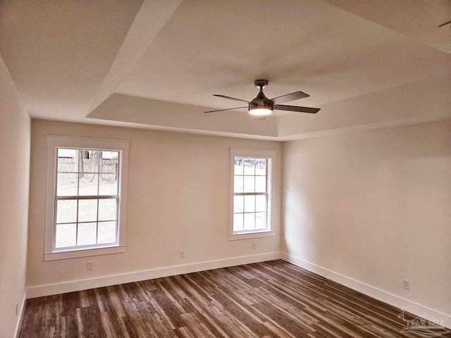 unfurnished room featuring dark wood-type flooring, a tray ceiling, and ceiling fan