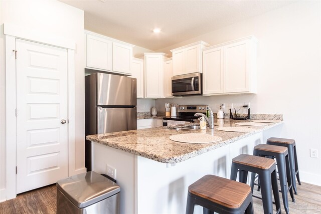 kitchen featuring white cabinets, dark hardwood / wood-style flooring, appliances with stainless steel finishes, and a kitchen bar