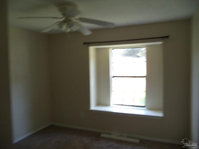 empty room with dark carpet, a wealth of natural light, and ceiling fan