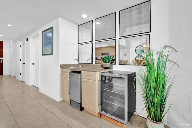 kitchen with beverage cooler, light stone counters, freestanding refrigerator, a sink, and light tile patterned flooring