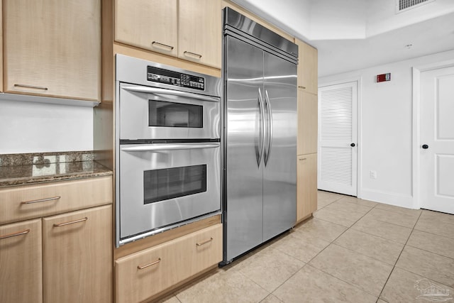 kitchen with light tile patterned flooring, light brown cabinets, visible vents, appliances with stainless steel finishes, and dark stone countertops