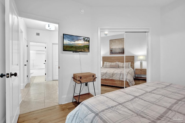 bedroom with connected bathroom, light wood-style flooring, visible vents, baseboards, and a closet