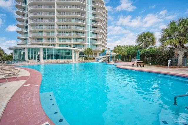 community pool with fence, a water slide, and a patio