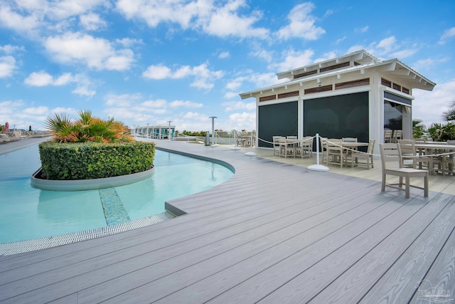 outdoor pool with outdoor dining space, a sunroom, and a deck with water view