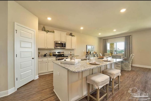 kitchen featuring stainless steel appliances, an island with sink, a breakfast bar, and white cabinetry