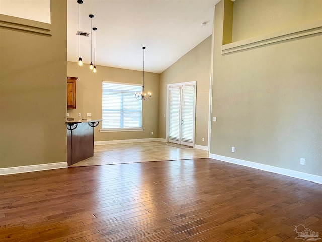 unfurnished living room featuring dark wood-type flooring, high vaulted ceiling, and an inviting chandelier