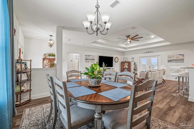 dining room with visible vents, ceiling fan with notable chandelier, a tray ceiling, and dark wood finished floors