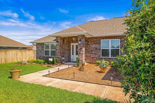 view of front of house with a front yard, fence, brick siding, and roof with shingles
