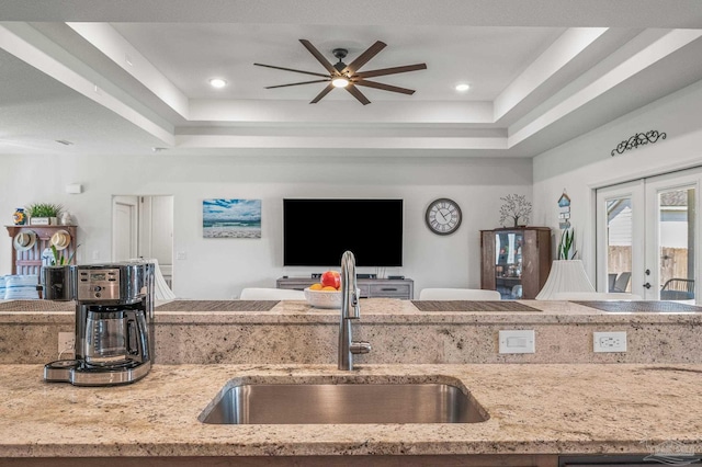 kitchen featuring a tray ceiling, open floor plan, a sink, and a ceiling fan