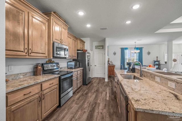 kitchen featuring dark wood finished floors, light stone countertops, a chandelier, a sink, and stainless steel appliances