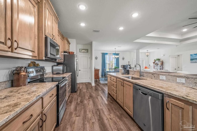 kitchen with appliances with stainless steel finishes, an inviting chandelier, light stone counters, dark wood finished floors, and a sink