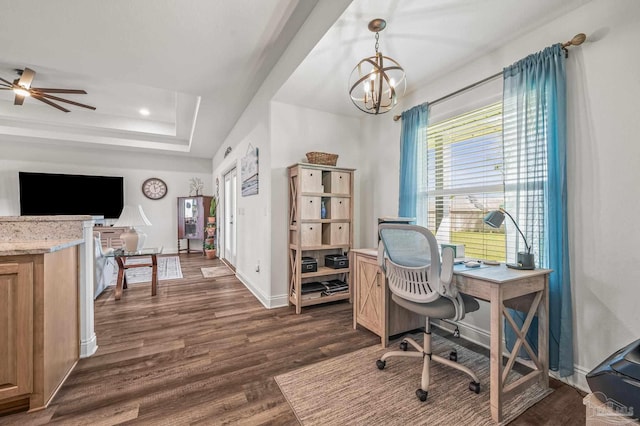 home office featuring dark wood-type flooring, ceiling fan with notable chandelier, a tray ceiling, and baseboards