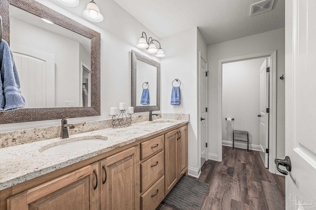 bathroom with double vanity, visible vents, a sink, and wood finished floors
