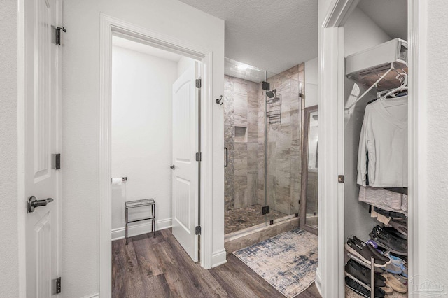 bathroom with a shower stall, a textured ceiling, wood finished floors, a walk in closet, and a wall mounted air conditioner