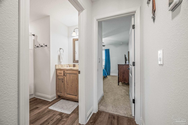 bathroom with a textured wall, vanity, baseboards, and wood finished floors