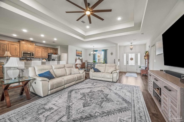 living area with recessed lighting, a tray ceiling, dark wood-style floors, and ceiling fan with notable chandelier