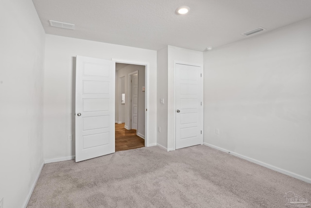 unfurnished bedroom with carpet, visible vents, a textured ceiling, and baseboards