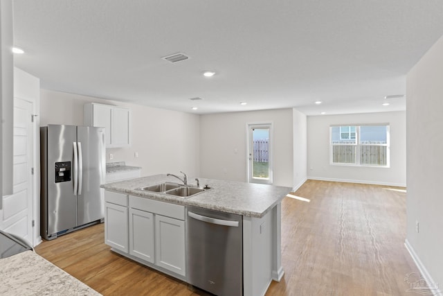 kitchen featuring stainless steel appliances, light wood-type flooring, a sink, and a center island with sink