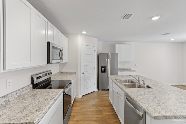 kitchen with light wood finished floors, a center island with sink, stainless steel appliances, light countertops, and a sink