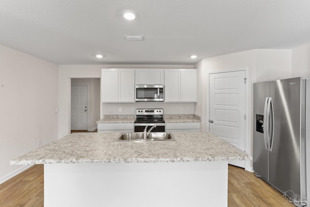 kitchen featuring white cabinetry, light countertops, appliances with stainless steel finishes, light wood-type flooring, and a center island with sink