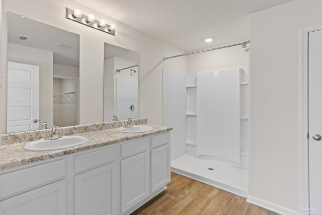 full bath with visible vents, a sink, a textured ceiling, wood finished floors, and walk in shower