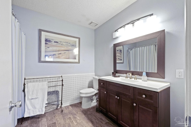 bathroom with a textured ceiling, toilet, vanity, tile walls, and hardwood / wood-style flooring