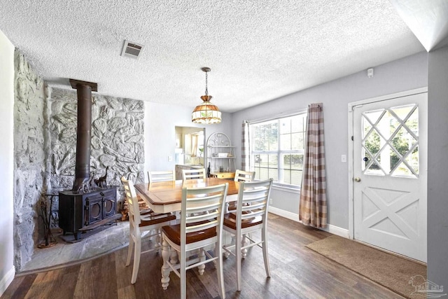 dining area with a textured ceiling, a wood stove, dark hardwood / wood-style flooring, and plenty of natural light