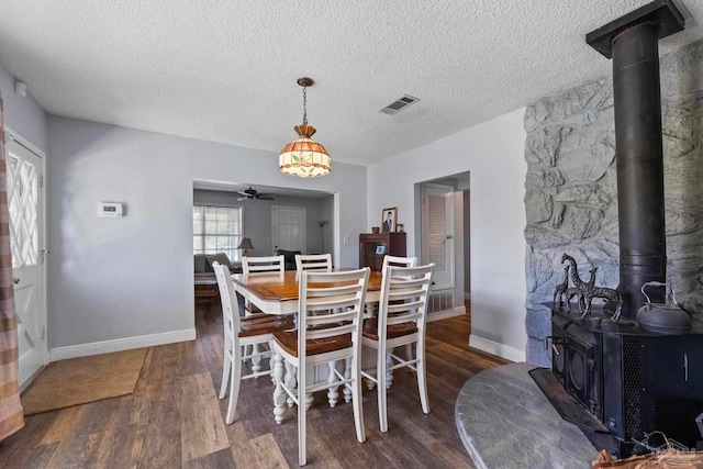 dining area with a textured ceiling, dark hardwood / wood-style flooring, a wood stove, and ceiling fan