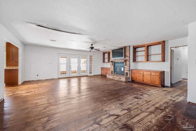 unfurnished living room featuring ceiling fan, a large fireplace, dark wood-type flooring, and a textured ceiling