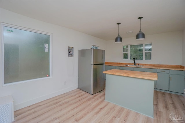 kitchen with sink, decorative light fixtures, stainless steel refrigerator, light wood-type flooring, and wood counters