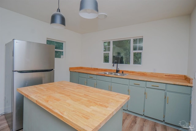 kitchen with stainless steel fridge, light wood-type flooring, decorative light fixtures, sink, and butcher block countertops