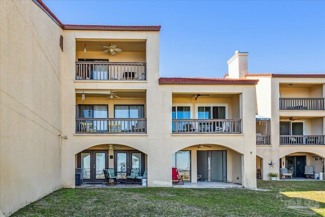 rear view of property with a lawn, a ceiling fan, a chimney, a patio area, and stucco siding