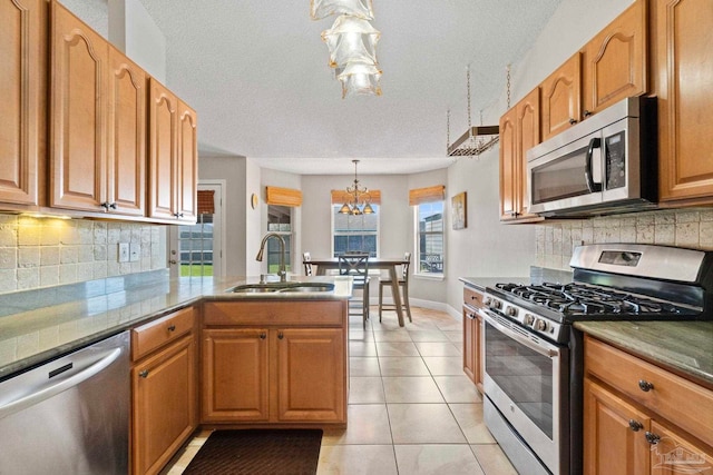 kitchen featuring light tile patterned flooring, a peninsula, a sink, appliances with stainless steel finishes, and tasteful backsplash