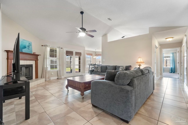 living area with light tile patterned floors, visible vents, a tiled fireplace, vaulted ceiling, and ceiling fan with notable chandelier