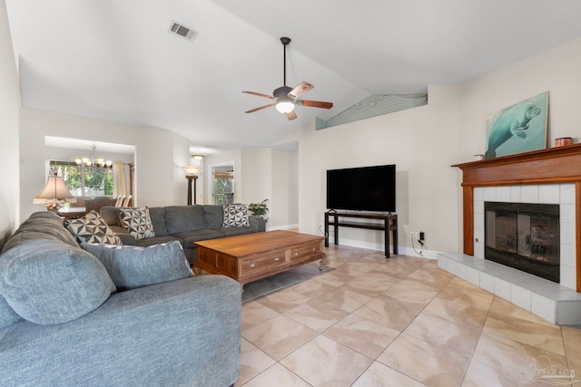 living area with ceiling fan with notable chandelier, lofted ceiling, visible vents, and a tile fireplace