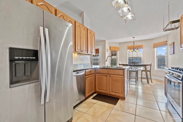 kitchen with light tile patterned floors, stainless steel appliances, a peninsula, a sink, and decorative backsplash