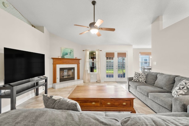 living room with lofted ceiling, ceiling fan, a tiled fireplace, and tile patterned floors