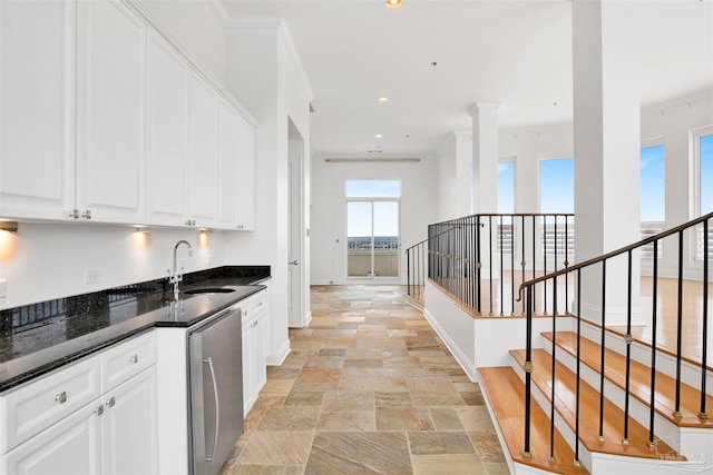 kitchen featuring ornamental molding, sink, stainless steel dishwasher, white cabinetry, and dark stone counters