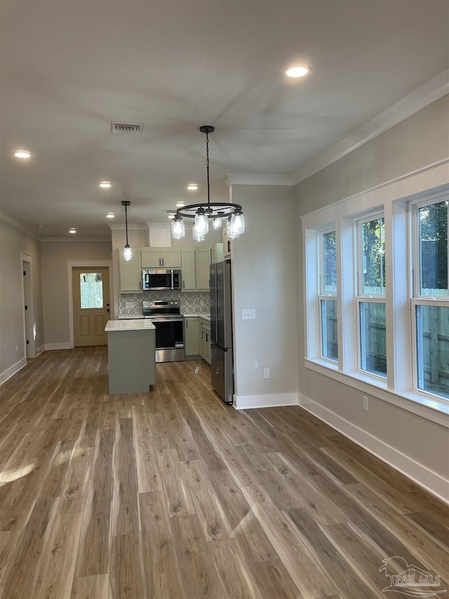 kitchen featuring tasteful backsplash, hanging light fixtures, a center island, stainless steel appliances, and crown molding