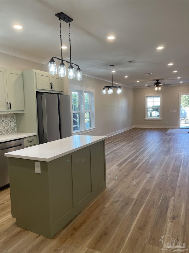 kitchen with appliances with stainless steel finishes, white cabinetry, hanging light fixtures, a center island, and light wood-type flooring