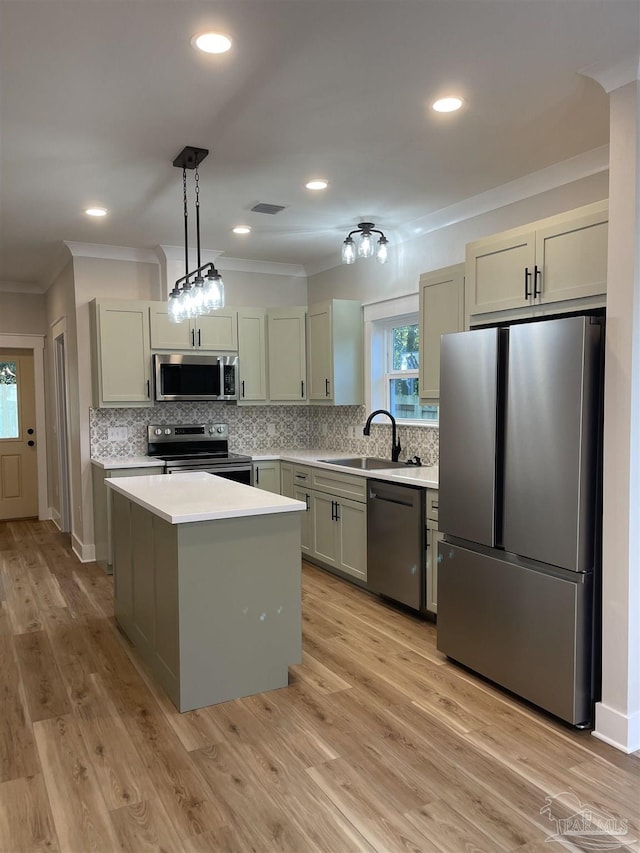 kitchen with appliances with stainless steel finishes, sink, hanging light fixtures, a center island, and light hardwood / wood-style flooring